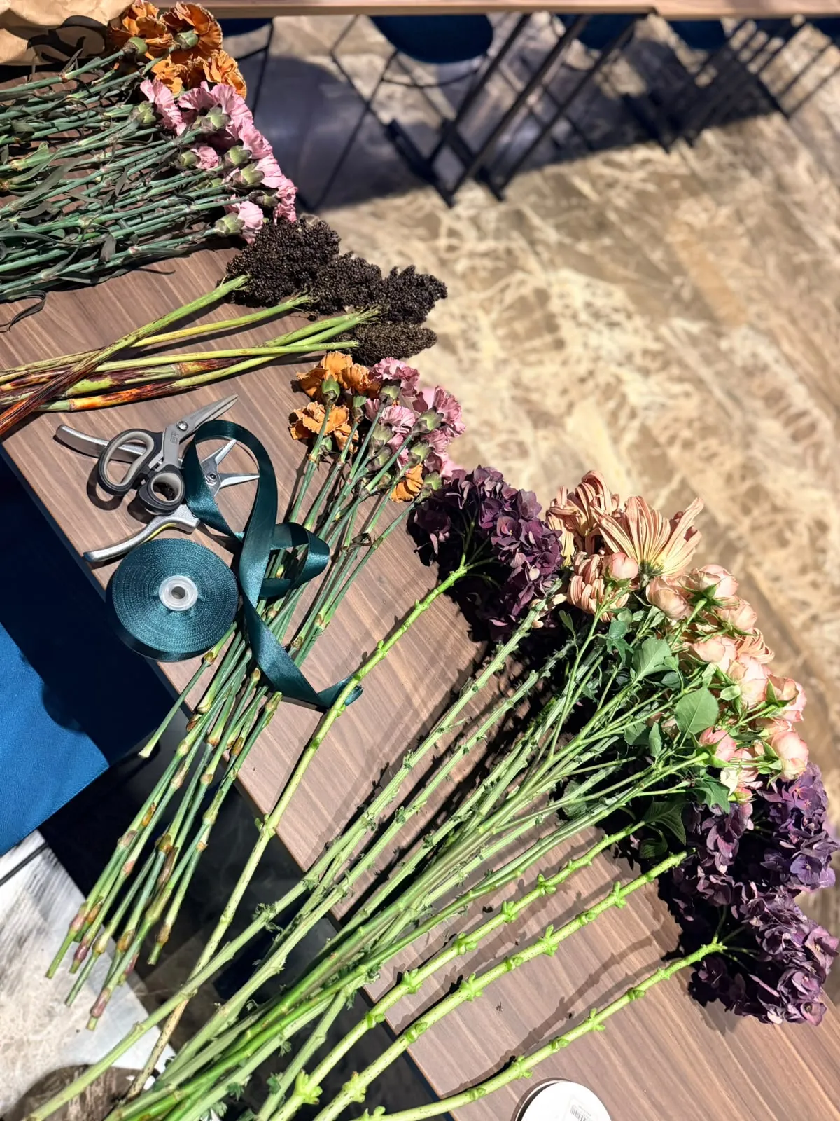 Fiori per il workshop sul tavolo: ortensie prugna, garofani ramati, forbici e nastro verde petrolio
